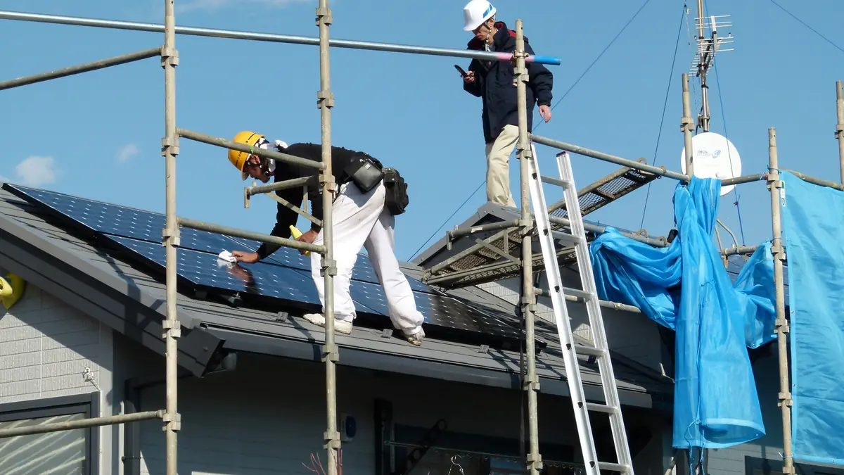 Installers on scaffolding fitting solar panels to a house roof